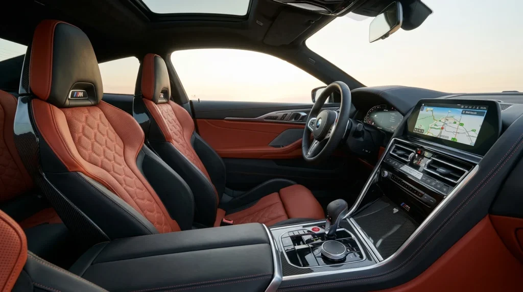 The interior cabin of a 2024 BMW M8 Competition featuring dual-tone leather seats and a carbon fiber center console.